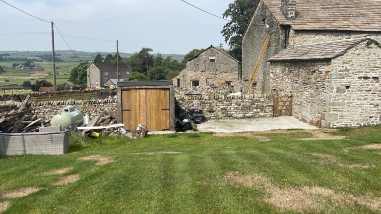 Barn and outside area of Middle Mearbeck Barn. Grass lawn and drystone walls.